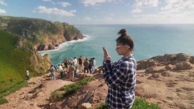 Bir kadın, okyanus manzarasıyla övünen manzaralı bir uçurumda dururken güzel anılar yakalar.