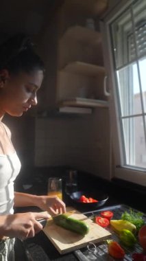 Odaklanmış bir birey, sağlıklı bir yaşam tarzını kucaklamak için parlak bir mutfakta renkli sebzeleri ustaca hazırlıyor.