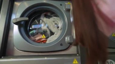 Çamaşır makinesini yakından izleyen genç bir kadın çamaşırlarını içeri dökerken, çamaşırlarını sergiliyor..