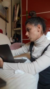 Dizüstü bilgisayarı üzerinde yoğun bir şekilde çalışan genç bir kadın ev ortamında verimlilik ve konsantrasyon gösteriyor..