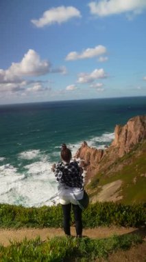 Bir insan kolları açık, nefes kesen bir sahil manzarasında duruyor, doğanın güzelliğini tamamen kucaklıyor.