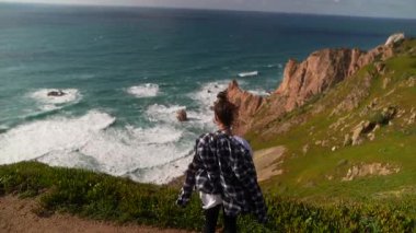 Huzurlu bir kıyı manzarası, nefes kesen okyanus manzarasının tadını çıkaran bir yürüyüşçüyü canlı bir şekilde yakalıyor.