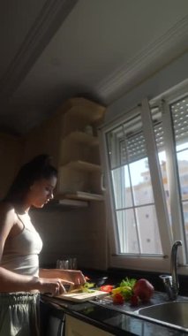 Bir kadın parlak, güneşli bir mutfakta taze sebzeleri ustalıkla hazırlıyor. Sağlıklı bir yaşam tarzını güzellikle somutlaştırıyor.