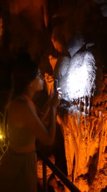 Meraklı bir birey loş bir mağarada akıllı telefon ışığı kullanırken karmaşık mağara oluşumlarını inceliyor.