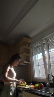 Bir kadın güneşli bir mutfakta çeşitli taze sebzeler hazırlamakla meşgul.