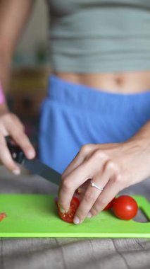 Renkli ve canlı yeşil bir kesme tahtasında taze, olgun domatesleri ustalıkla dilimleyen bir elin yakından görüntüsü.