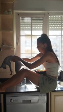 Neşeli bir kadın mutfak tezgahında lezzetli kahvaltısını yaparken neşeli evcil hayvanı da ona katılıyor.