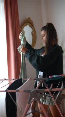 Genç bir kadın evde yeni yıkanmış giysileri dikkatlice düzenliyor, rahat bir ortam yaratıyor ve yayıyor.