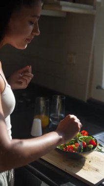 Bir kadın güneşli bir mutfakta taze bir salata hazırlıyor, canlı malzemeler sergiliyor ve sağlıklı besleniyor..
