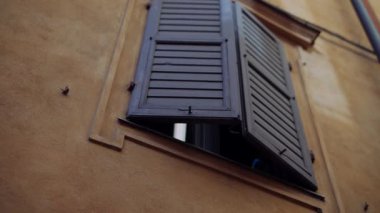 Zarif ahşap panjurlar, kırsal bir İtalyan duvarına karşı açılıyor ve mimari güzelliğini güzelce sergiliyor.