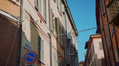 Güzel ve canlı bir İtalyan sokak sahnesi açık mavi gökyüzünün altında renkli binalar sergiliyor.