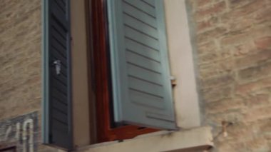 Canlı yeşil ağaçları ve büyüleyici mavi kepenkleri olan taşralı tuğlalı duvarı olan pitoresk bir sokak manzarası.