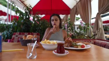 Genç bir kadın, canlı dekorlarla süslenmiş sıcak bir açık hava restoranında lezzetli ve tatmin edici bir yemeğin tadını çıkartıyor.