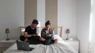 Bir çift, rahat yataklarında, modern yatak odasındaki aletleriyle meşgul olarak, kaliteli vakit geçirmekten mutlu olurlar.