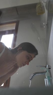 Huzurlu ve aydınlık bir banyoda, bir insan yüzünü yıkamak ve kendini yenilemek için zaman ayırır.