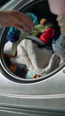 Bir el, çamaşırları yıkamak için çeşitli renkli giysiler ve battaniyeleri dikkatlice çamaşır makinesine yerleştirir.