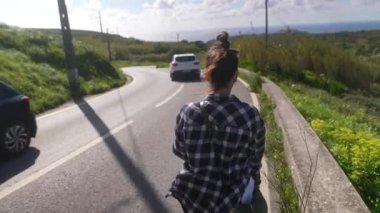 Canlı yeşillikler ve parlak mavi gökyüzü ile çevrili, güzel, resimli bir yol boyunca sakin bir şekilde yürüyen bir insan.