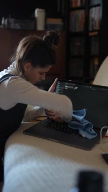 Sıcak bir ev ortamında, bir kadın mikrofiber bez kullanarak özenle dizüstü bilgisayarını temizlerken odaklanır.