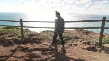 Bir kadın, engin okyanusa bakan bir uçurumun kıyısında durarak huzurlu ve huzurlu bir anı yaşıyor.