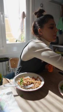 Genç bir kadın, besleyici ve lezzetli bir yemeğin tadını çıkarırken güneşli bir mutfak masasında sıcaklığın tadını çıkarıyor.