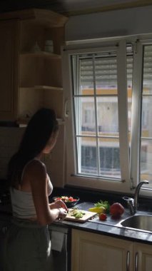 Bir kadın aydınlık, güneşli bir mutfakta taze sebzeler hazırlıyor ve yemek pişirme sürecinin her anının tadını çıkarıyor.
