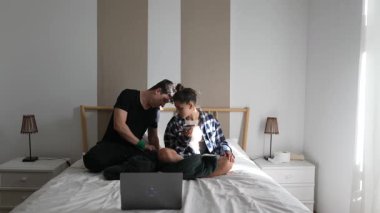 Bir çift, neşeli evcil hayvanlarının yanında dizüstü bilgisayar kullanarak yatak odalarında güzel vakit geçirmekten mutlu olurlar.