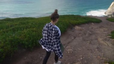 Genç bir kadın resmedilmeye değer bir sahil yolunda yürüyor, etrafındaki çarpıcı okyanus manzarasının tadını çıkarıyor.