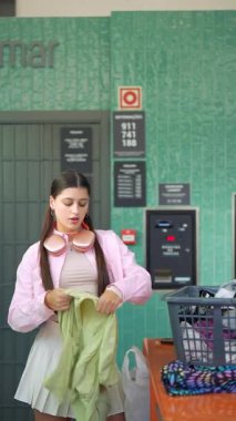 Genç bir kadın şık bir çamaşırhanede yeşil çamaşırları sınıflandırıyor, canlı ve enerjik bir atmosferi yansıtıyor.