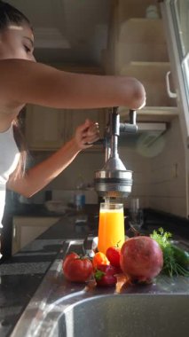 Parlak ve güneşli bir mutfakta genç bir kadın renkli meyvelerden taze meyve suyu hazırlar.