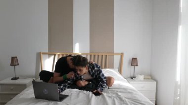 Sıcak bir yatak odasında, genç bir çift laptoplarını birlikte kullanırken sevgi dolu bir şekilde iletişim kuruyor.