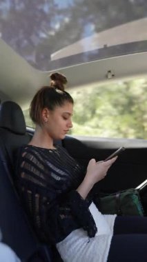 Genç bir kadın şık bir arabanın içinde modern yaşam tarzını sergileyerek akıllı telefonuna odaklanır..