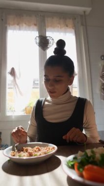 Neşeli bir kadın canlı ve besleyici bir yemekten zevk alıyor. Parlak, güneşli bir mutfak ortamında rahat bir yerde.