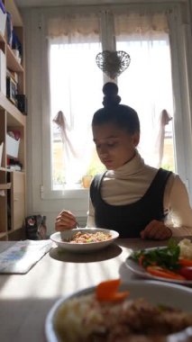 Genç bir kadın, çeşitli lezzetli yemek seçenekleriyle çevrili, parlak bir mutfak masasında yemeğinin tadını çıkarıyor.