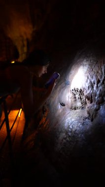 Meraklı bir ziyaretçi, loş bir mağarada akıllı bir telefonla aydınlatılan çarpıcı antik mağara sanatını ayrıntılı bir şekilde inceliyor.