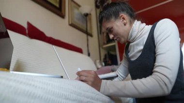 Düşüncelere dalmış genç bir kadın dizüstü bilgisayarıyla rahat bir koltukta otururken yaratıcı bir şekilde yazar.