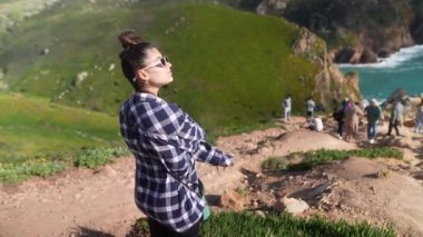 Bir kadın nefes kesici bir uçurumun kenarında duruyor, yemyeşil kıyı manzarasına hayran.