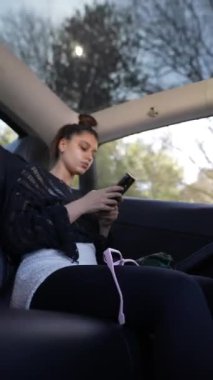 Genç bir kadın arabasında rahat bir şekilde otururken, dışarıdaki güzel manzaranın tadını çıkarırken, akıllı telefonuna derinden odaklanıyor.