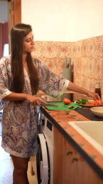 Mutfağında, rahat bir bornoz giyen bir kadın yemeği için taze, renkli sebzeleri titizlikle doğruyor.