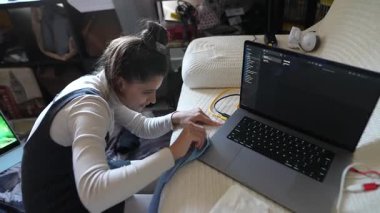 Dizüstü bilgisayar kullanırken dikiş işi yapan, sanatsal yeteneklerini modern teknolojiyle harmanlayan biri.