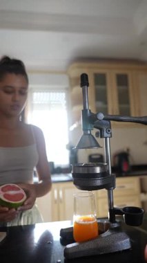 Şık ve modern mutfağında genç bir kadın büyük bir özenle taze narenciye suyu hazırlıyor.