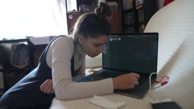 Dizüstü bilgisayarına derinden odaklanan genç bir kadın rahat ve evine davet edici bir çevrede, işine dalmış.