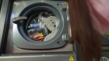 Çamaşır makinesini yakından izleyen genç bir kadın çamaşırlarını içeri dökerken, çamaşırlarını sergiliyor..