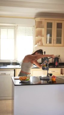 Bir kadın güneşli bir mutfakta taze meyve suluyor, sağlıklı yaşam tarzı ve canlı yemek hazırlığı sergiliyor..