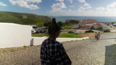 Meraklı bir turist, sakin bir kıyı manzarasına bakan güzel bir kaldırım taşı yolu boyunca düşünceli bir şekilde yürür.