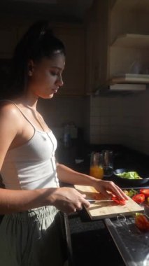 Genç bir kadın, güneşli bir mutfak alanında çeşitli renkli sebzeleri ustalıkla doğruyor.