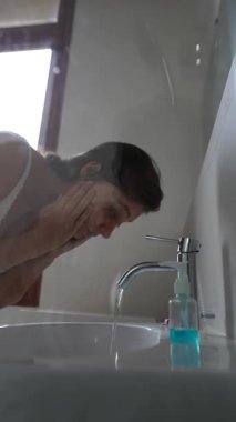 Bir insan nazikçe yüzünü lavaboda yıkar. Deriyi besleyen huzurlu bir sabah rutinini resmeder.