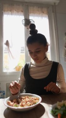 Genç bir insan güneşli bir mutfak masasında her lokmanın tadını çıkarıyor.