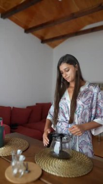 Bir kadın kahvesini evde demliyor. Rutinindeki huzurlu rahatlama ve kasıt anlarını yakalıyor.