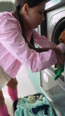 Canlı bir çamaşırhane ortamında, genç bir kadın giysilerini bir çamaşır makinesine yüklerken mutlu oluyor.
