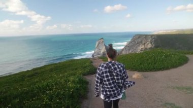 Bir gezgin, nefes kesen okyanus manzarası ve görkemli uçurumlarla çevrili manzaralı bir sahil yolunda yürüyor.